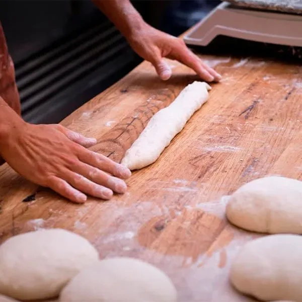 Manos estirando la masa junto a varias bolas ya formadas