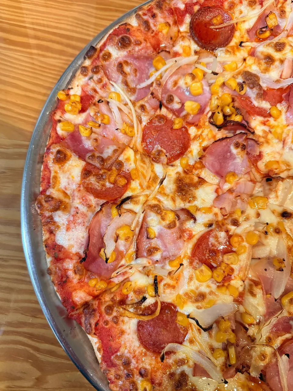 Detalle de una pizza con jamón, pepperoni, maíz y cebolla, con el queso gratinado